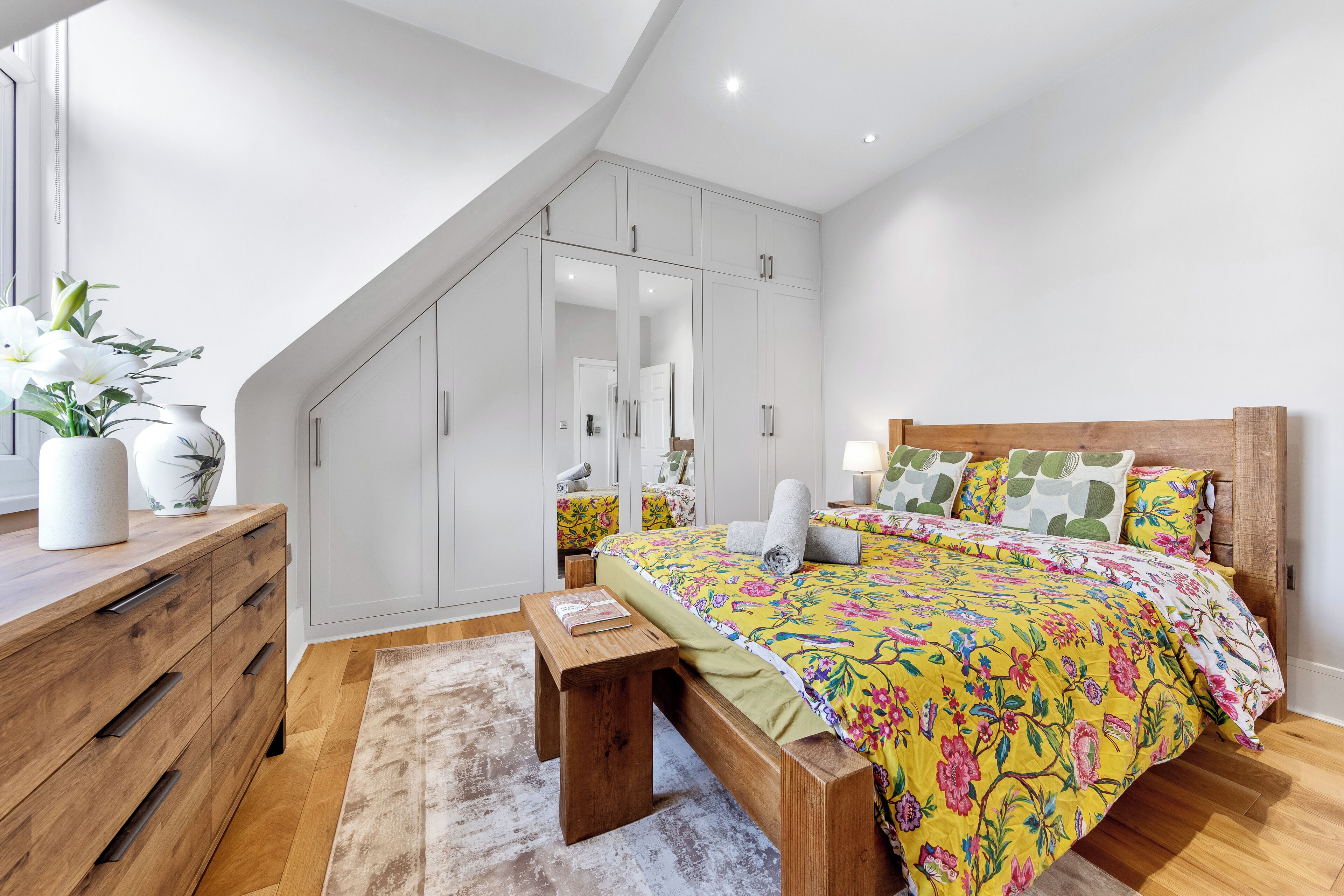Une chambre à coucher avec un lit en bois, une commode en bois, un banc, un miroir et une armoire.
