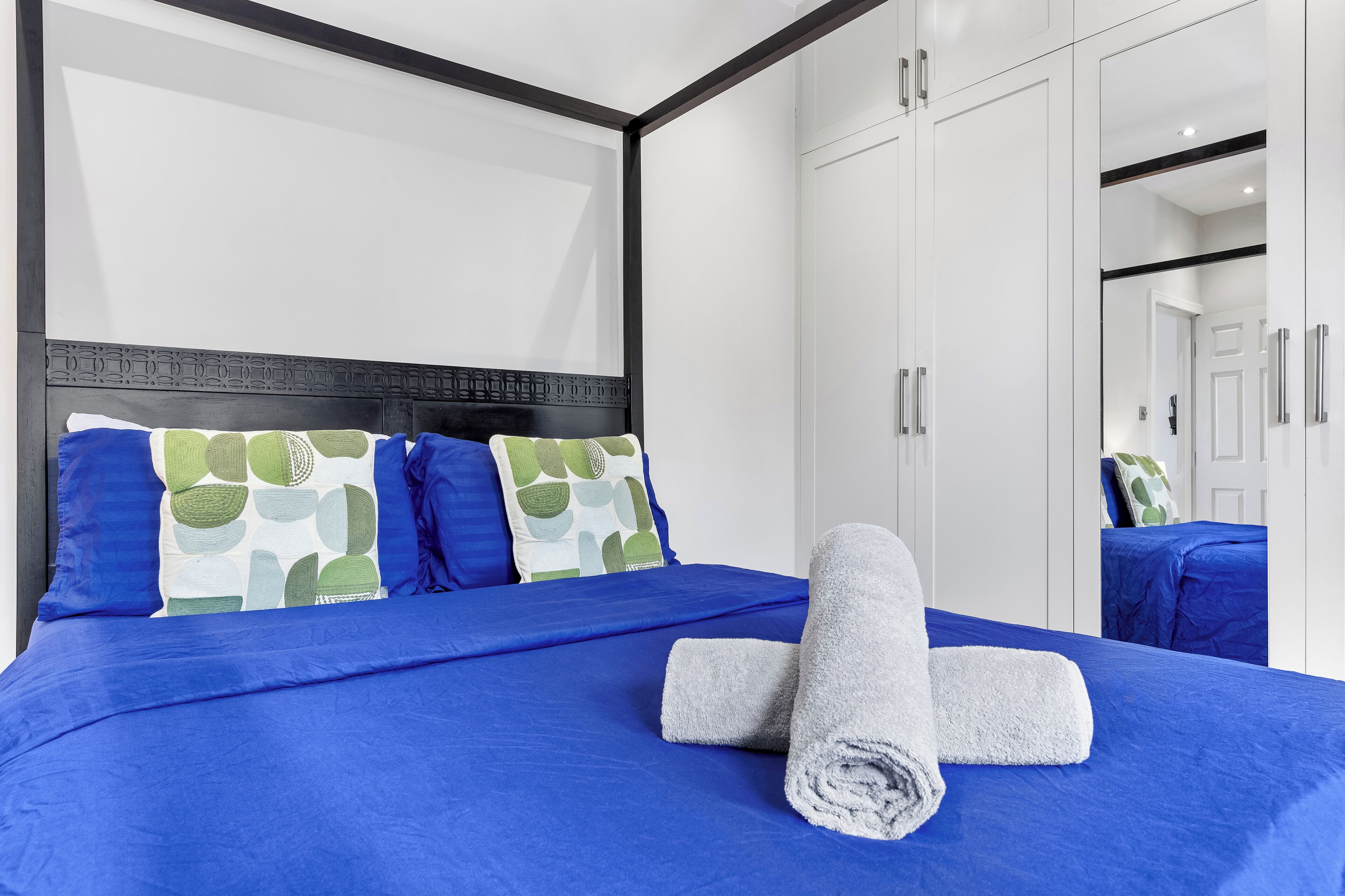 A hotel room with a large bed, a headboard with a geometric pattern, white wardrobes, and a mirror reflecting the room.