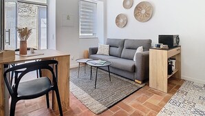 A modern living room with a grey sofa, a wooden side table, a small coffee table, and a decorative wall hanging. - CASA BEIRA-MAR - Charming typical Moradia house in OLHAO -ROOFTOP and parking lot (Olhão)