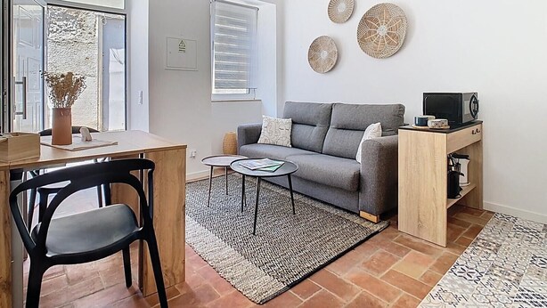 A modern living room with a grey sofa, a wooden side table, a small coffee table, and a decorative wall hanging. - CASA BEIRA-MAR - Charming typical Moradia house in OLHAO -ROOFTOP and parking lot (Olhão)