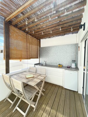 Un terrazzo in legno con tavolo e sedie, una zona cottura con lavello e piano di lavoro, e una finestra vista terrazzo.