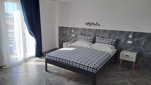 Une chambre à coucher comprenant un lit, deux tables de chevet, une étagère fixée au mur et une fenêtre avec des rideaux.