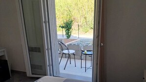 Une chambre avec un grand lit et une porte-fenêtre coulissante donnant sur une terrasse extérieure équipée d’une table et de chaises.