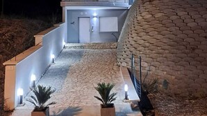 Un bâtiment moderne à deux étages, doté d’un mur en pierre et d’un espace d’entrée pavé agrémenté de plantes en pot.
