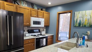 Una cocina con encimeras de granito, electrodomésticos de acero inoxidable, armarios de madera, un microondas, una estufa y una ventana con vistas.