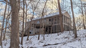 Una casa grande de varios pisos con un balcón, rodeada de árboles y cubierta de nieve.