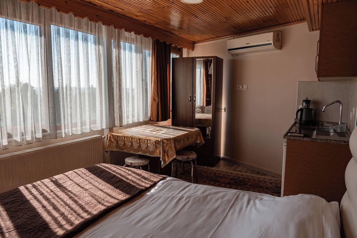 A bedroom with a bed, a table, a chair, a mirror, a sink, and an air conditioning unit.