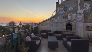 Eine Dachterrasse mit Korbmöbeln, einem Backofen und verschiedenen Schildern sowie Graffiti an den Wänden.