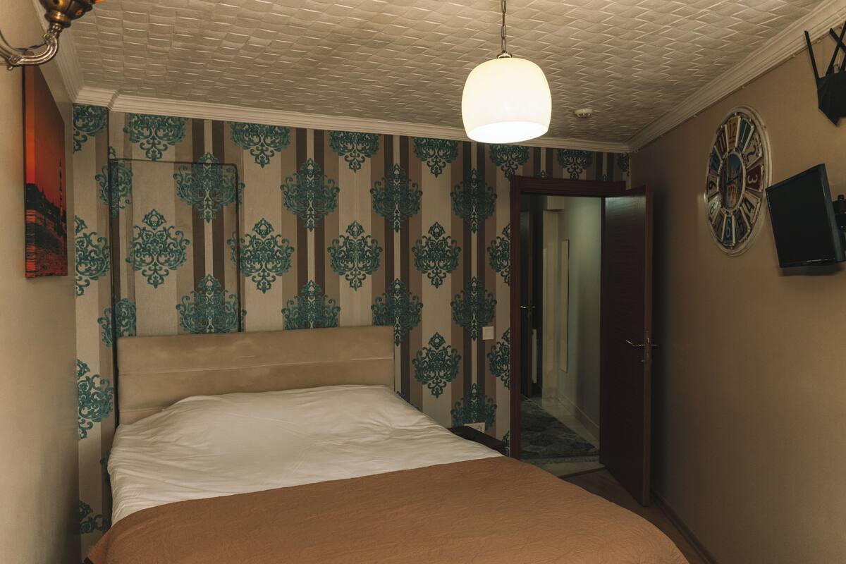A bedroom with a large bed, a clock on the wall, and a door leading to another room.