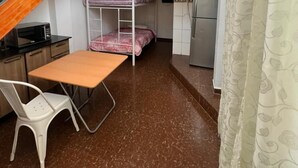 A compact dormitory room with bunk beds, a kitchenette, a small table, and a staircase.