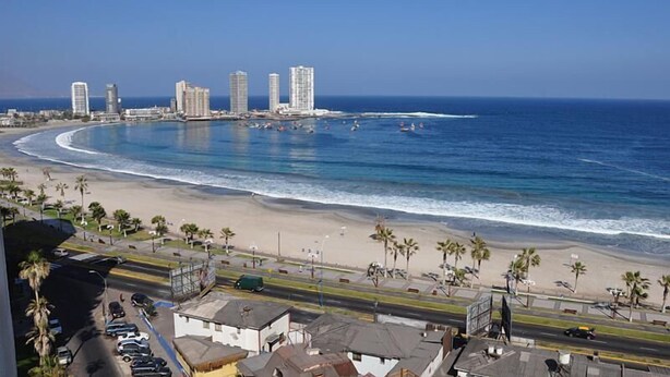A coastal cityscape with a beach, high-rise buildings, and a clear blue sky.