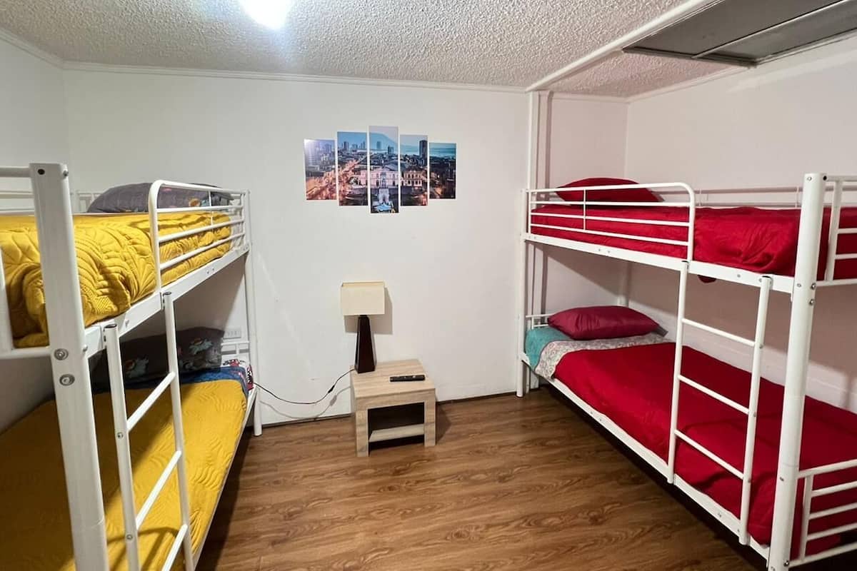 Une chambre de dortoir avec des lits superposés, une petite table avec une lampe et un mur orné d’une photographie représentant un paysage urbain.