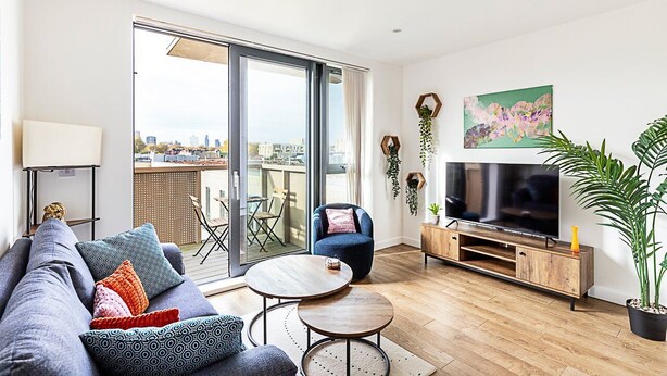 En moderne stue med sofa, sofabord, fjernsyn og balkon med udsigt over byen.