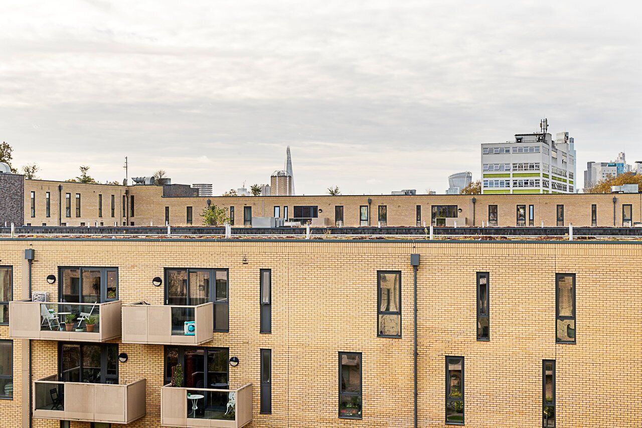 A multi-story building with a brick facade, multiple balconies with wicker furniture, and a view of a tall building in the background.