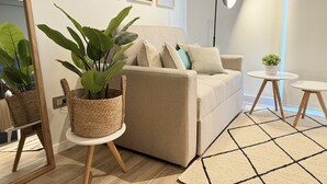 Una sala de estar con un sofá color beige, un espejo grande, una lámpara de pie y una mesita con una planta.