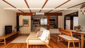 A spacious living room with wooden floors, a sofa, a TV, and a dining area with a table and chairs. - Private villa only a short stroll to the beach/Organic shop (Cobano)