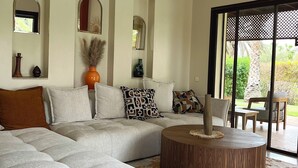 A modern living room with a sectional sofa, a round wooden coffee table, and a large sliding glass door leading to an outdoor area. - Fabulous family villa in Marrakech (Marrakech)