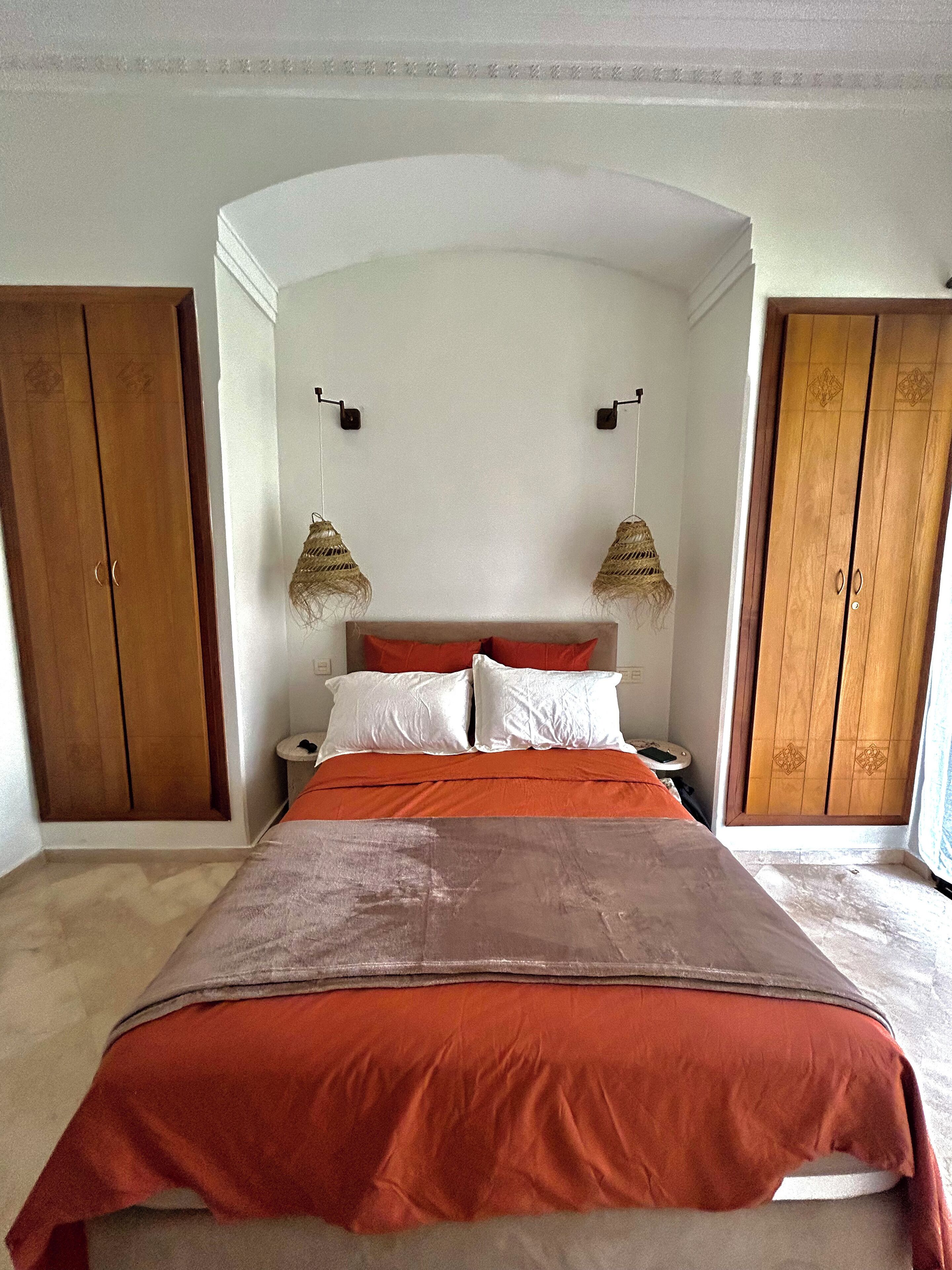 A bedroom with a large bed, two nightstands, a wooden wardrobe, and a hanging lamp.