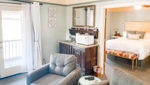 A hotel room with a bed, a desk, a chair, a small table, a mirror, and a window with curtains.