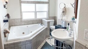 A bathroom with a freestanding bathtub, a toilet, a sink, and a window above the bathtub.