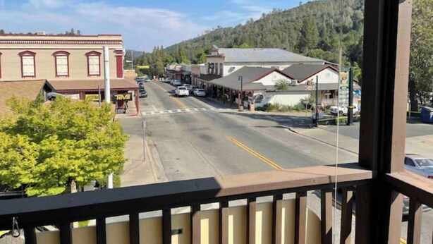 A street view with buildings, a clear sky, and a forested hill in the background.
