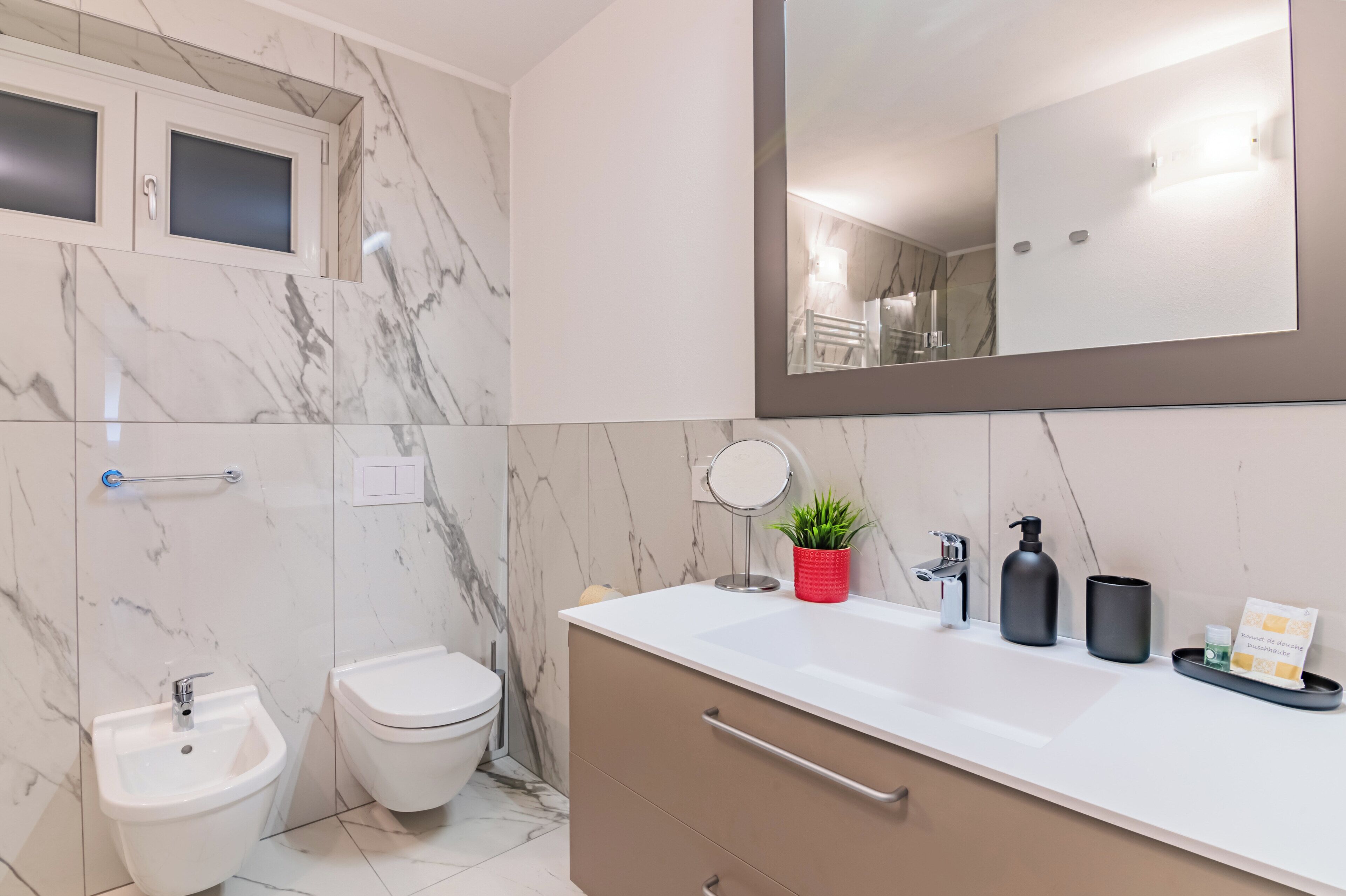 A modern bathroom with a marble backsplash, a large mirror, a sink, a toilet, and a bidet.