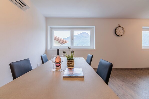 A conference room with a long table, four chairs, a clock on the wall, a window with a mountain view, and a potted plant.