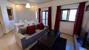 A modern living room with a sofa, dining table, and a TV. - Naxxar 3-Bedroom Spacious Family Home with Private Roof by Malta Weekend (Naxxar)