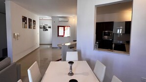 A modern kitchen with a built-in oven and microwave, a dining area with a white table and chairs, and a hallway with a red-framed window. - Naxxar 3-Bedroom Spacious Family Home with Private Roof by Malta Weekend (Naxxar)