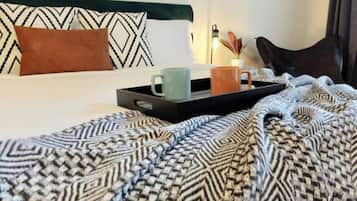 A neatly made bed with patterned bedding, a tray with two mugs, and a pillow on a headboard.