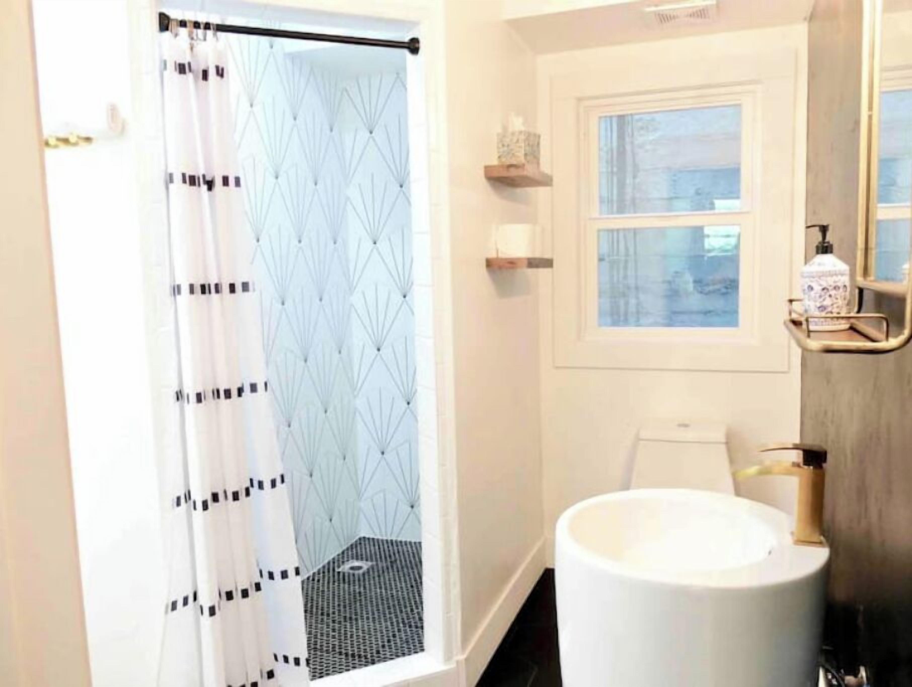 Een badkamer met een wit bad, een raam met uitzicht en een douchegordijn met een geometrisch patroon.