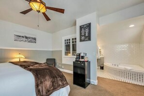 A hotel room with a bed, a desk, a refrigerator, a coffee maker, a window, and a bathroom with a bathtub.