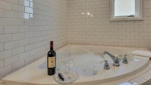 A bathroom with white tiled walls, a bathtub with a faucet, a wine bottle, and a wine glass.