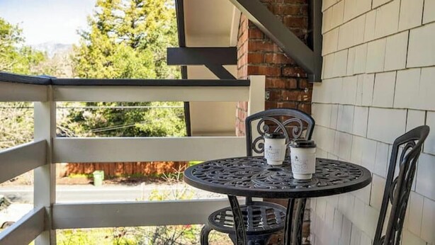 A balcony with a table and chairs, a brick wall, and a view of trees and mountains.