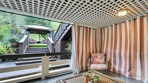 Un espace extérieur abrité, aménagé avec une table en osier, des rideaux à rayures et une chaise.
