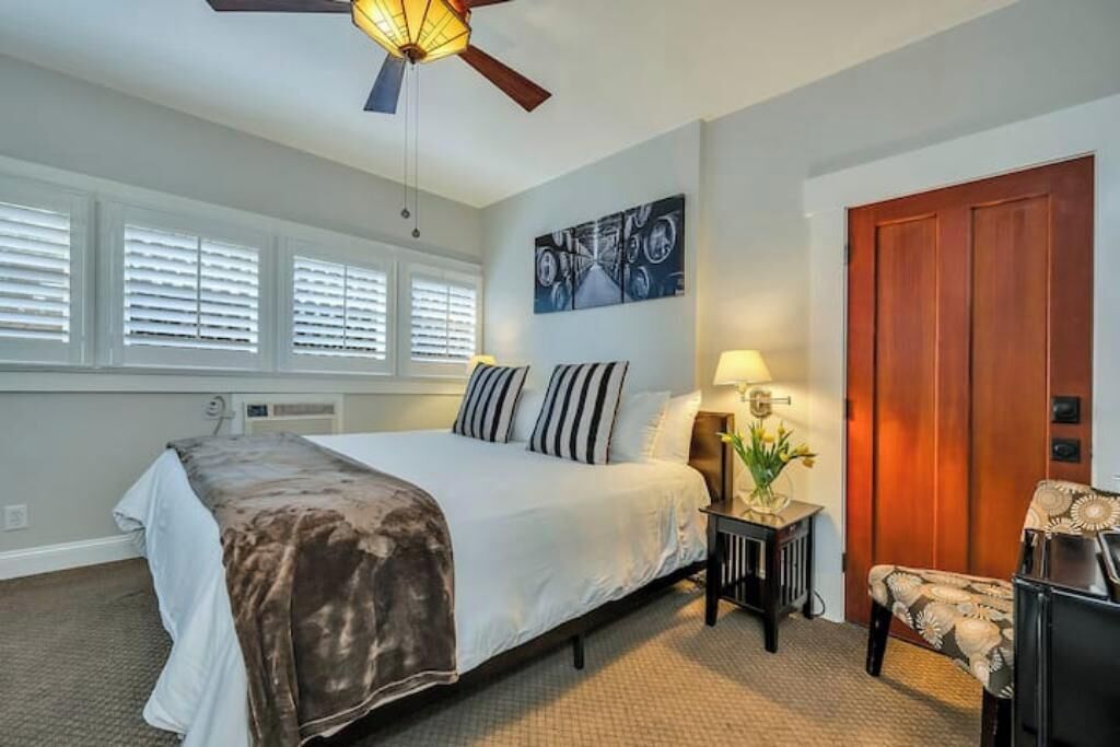 Un dormitorio con cama, mesita de noche, una silla, una puerta de madera y un ventilador de techo.