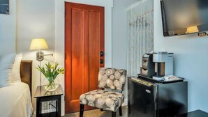 Une chambre d’hôtel avec un lit, une chaise, une machine à café, une télévision et une porte.