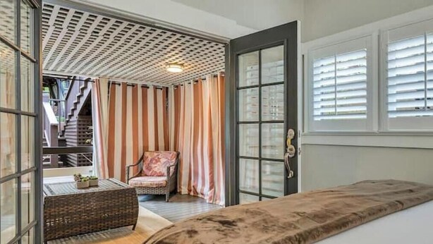 Une chambre avec un grand lit, une chaise en osier, une petite table et une vue sur un escalier.