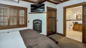 Een slaapkamer met een bed, een open haard, een televisie en een badkamer zichtbaar door een open deur.