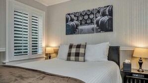 A hotel room with a large bed, two bedside tables, a wall-mounted artwork of barrels, and a window with blinds. - Charming Queen Room near Downtown Calistoga. (Calistoga)