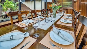 A dining table set with white plates, cutlery, and wine glasses, surrounded by wooden chairs. - Luxury King Room. Steps to Napa Valley Wineries, Spas & Fine Dining! (Calistoga)
