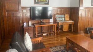 Une pièce aux murs lambrés, dotée d’un grand téléviseur à écran plat, d’un bureau en bois, d’un fauteuil rembourré et d’une table à manger.