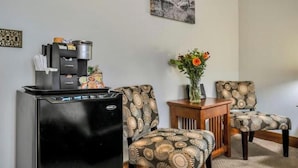 Un espacio habitable compacto con cafetera, dos sillas estampadas, una mesita de madera y un florero con flores.