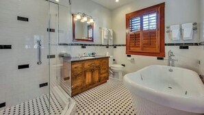 A bathroom with a glass shower enclosure, a wooden vanity, a freestanding bathtub, and a large mirror with lights.