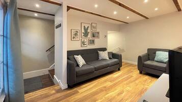 Uma sala de estar moderna com dois sofás cinza, piso de madeira e uma escada que leva a outro cômodo.