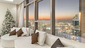 Un salon moderne avec un canapé blanc, de grandes fenêtres et une vue sur le paysage urbain au coucher du soleil.
