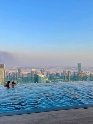 Vue sur la ville depuis une piscine à débordement où deux personnes se détendent.
