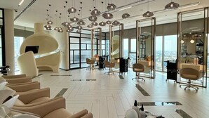 Un hall d’hôtel moderne doté d’un vaste espace salon, de plusieurs postes de coiffure et de grandes fenêtres offrant une vue sur la ville.