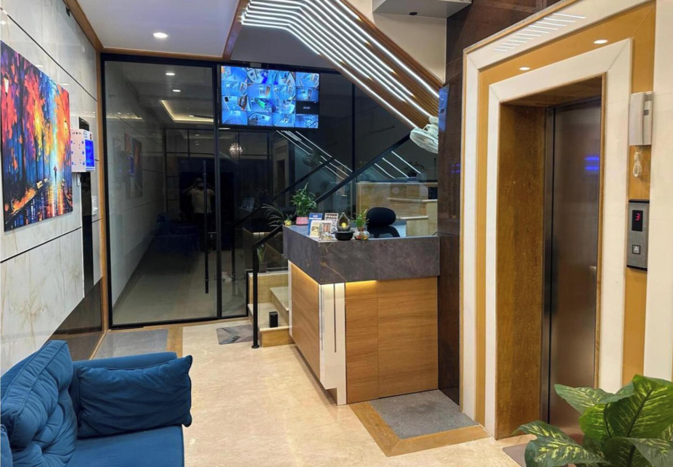 Un moderno vestíbulo de hotel con un mostrador de recepción, un sofá azul, una escalera y una pantalla de televisión que muestra diversas imágenes.