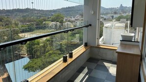 A balcony with a glass railing, a view of a cityscape, and a small wooden cabinet. - THE VP RESIDENCY TOWERRS (Thiruthani)